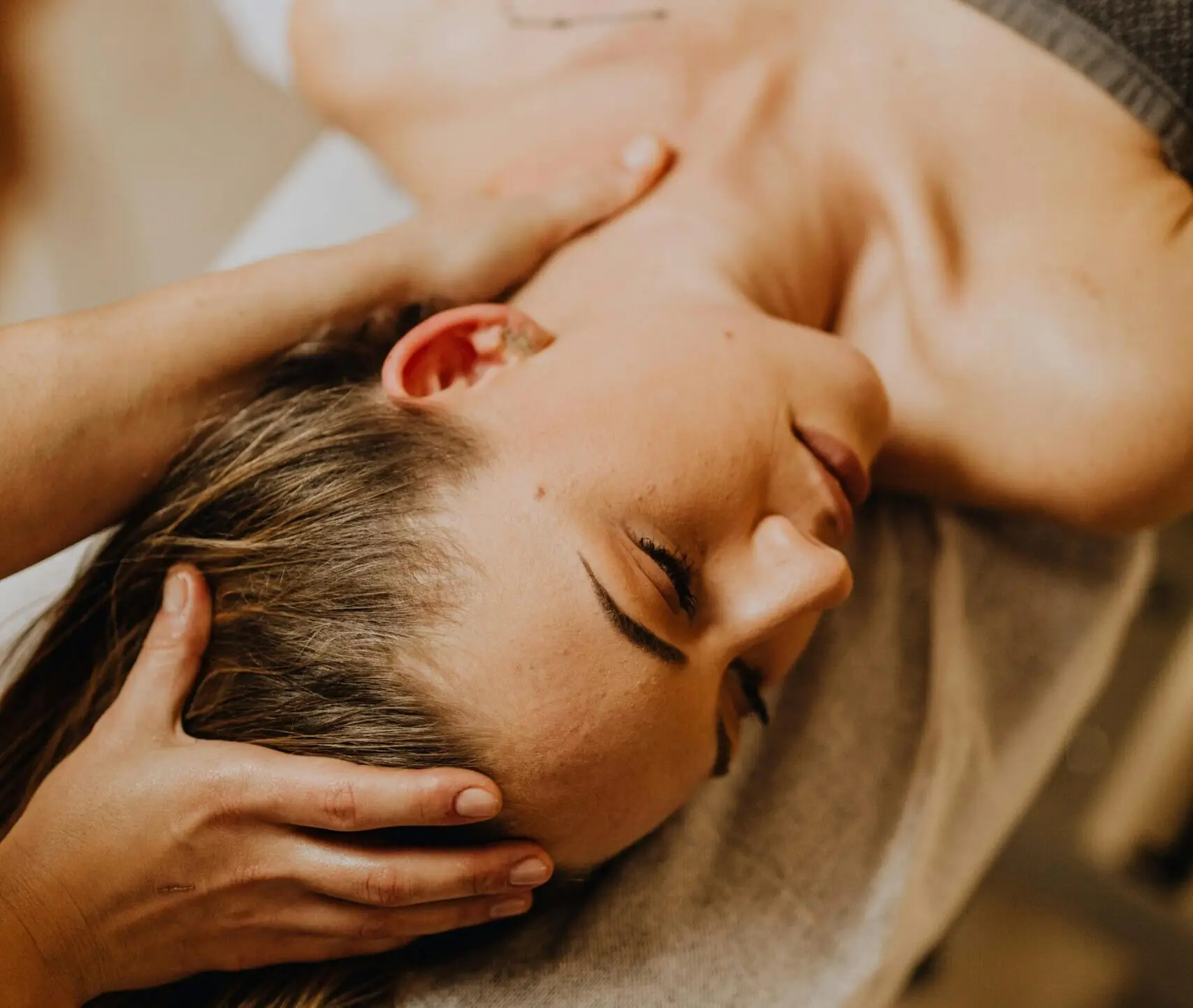 A woman receiving a head and neck massage in a serene spa setting, promoting relaxation and wellness.